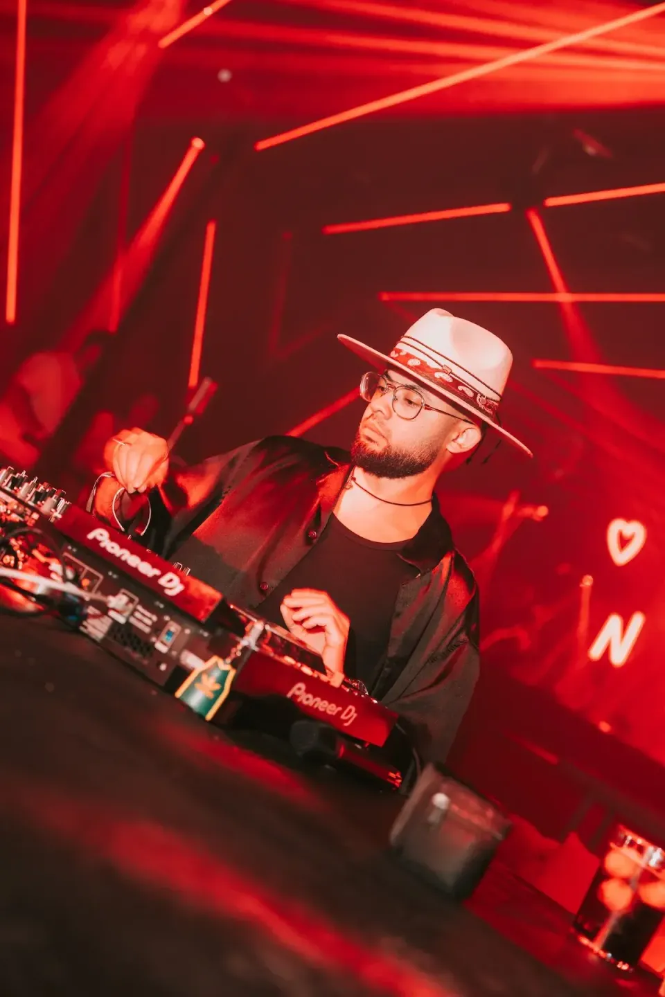DJ con sombrero pinchando en la cabina, bajo los láseres rojos