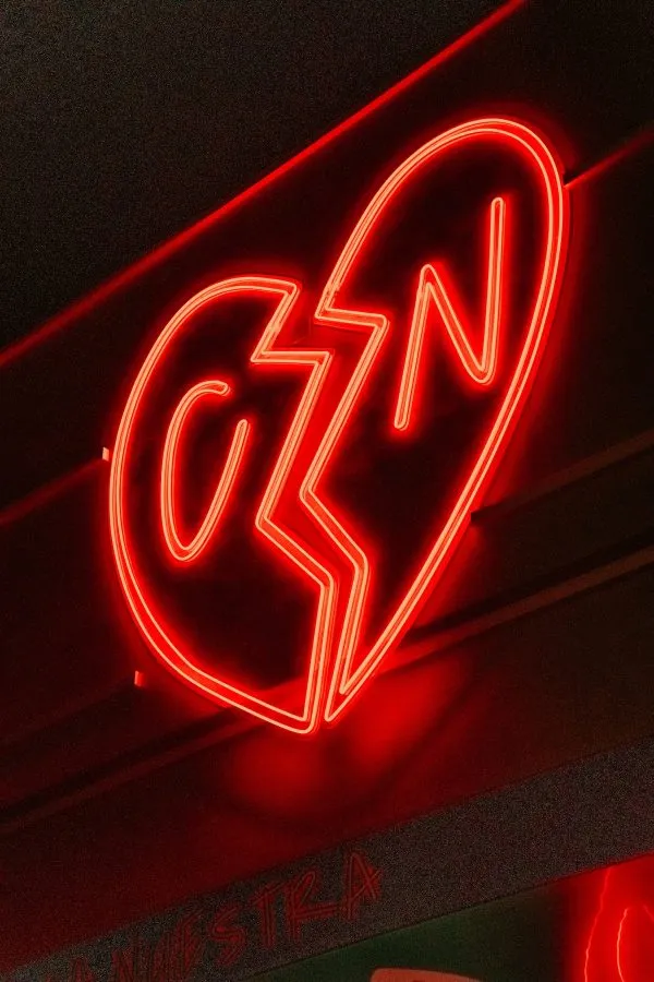 Corazón roto de neón rojo con las letras C y N en la pared de la sala